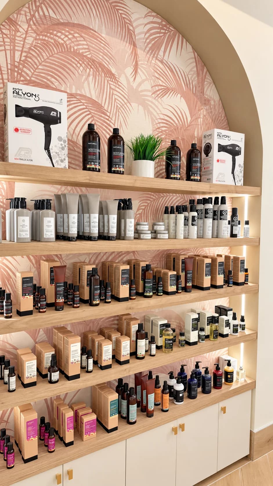 Professional haircare bottles and boxed products on wood shelves against pink botanical wallpaper