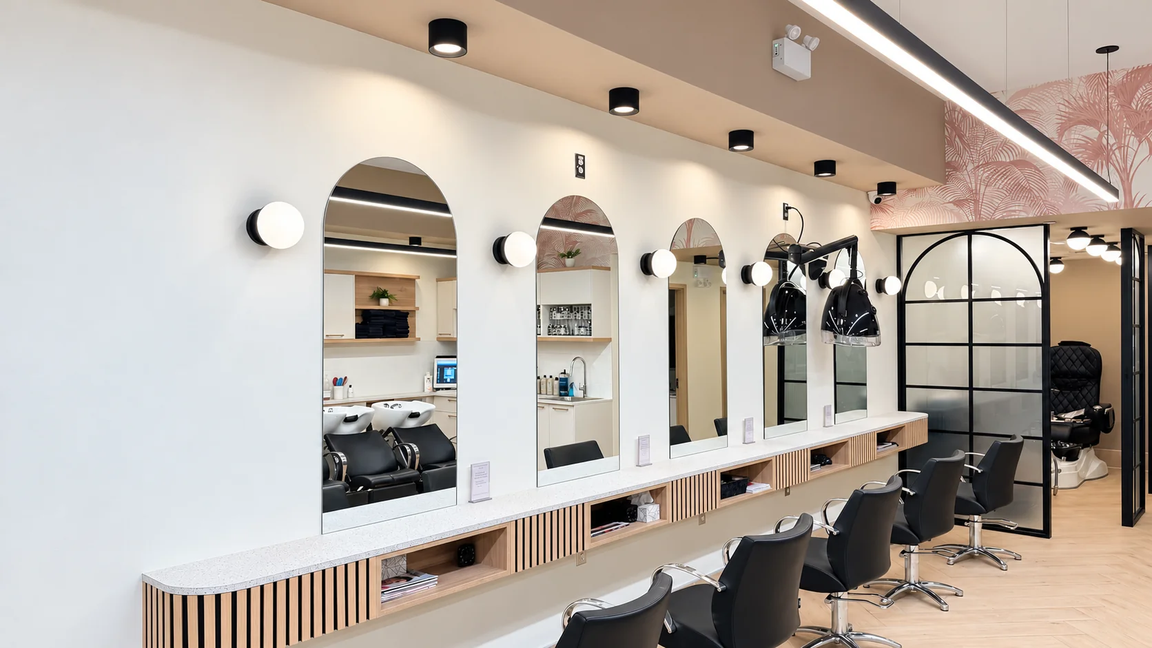 Row of empty styling chairs beneath arched mirrors and globe lights beside a black glass partition